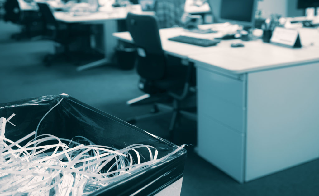 Shredded paper in a bin with blurred open space modern office in background - Documents destroyed by company staff during competition authorities dawn raid